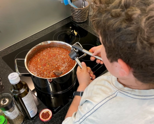 Ein Kind presst den Knoblauch in die Bolognese