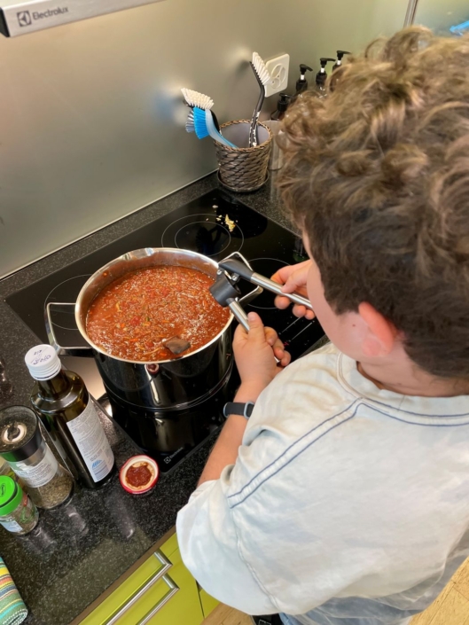 Ein Kind presst den Knoblauch in die Bolognese