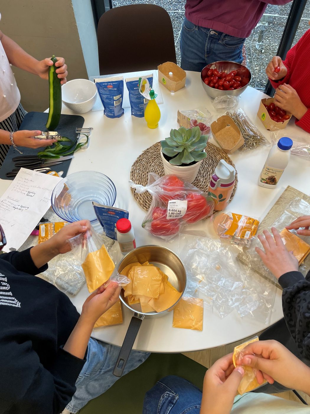 Kinder sitzen um runden Tisch und bereiten Käsesauce und Gemüsesticks vor