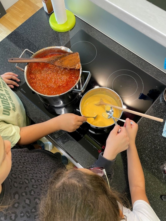 Kinder bereiten die Käsesauce und die Bolognese auf dem Herd vor