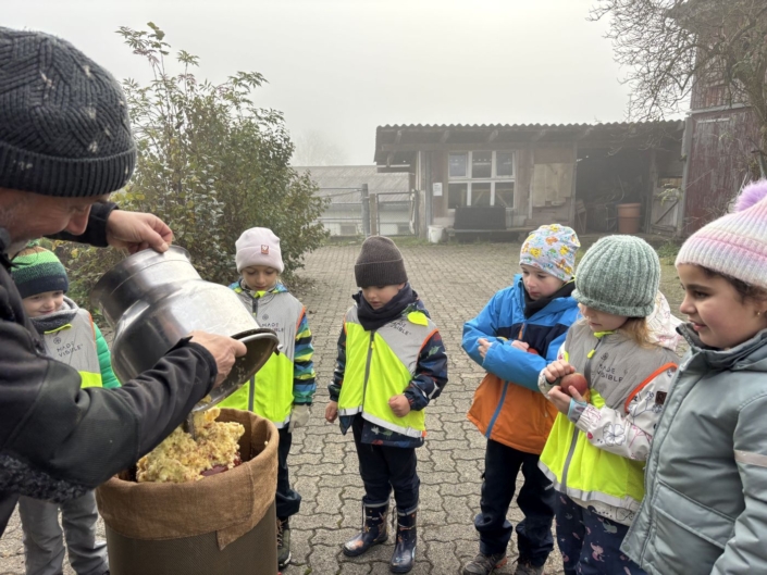 Der Bauer schüttet Rührei in einen anderen Behälter, während die Kinder gespannt zuschauen